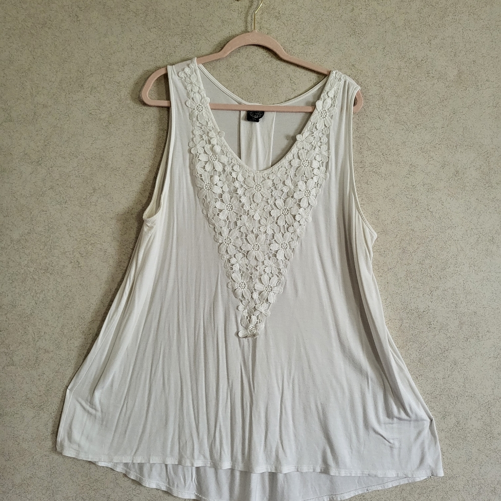 Long, sleeveless white blouse with floral detailing in the chest.